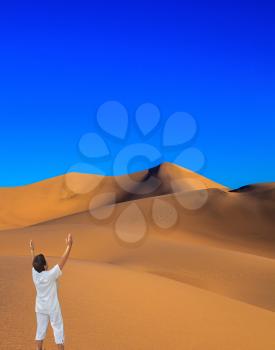 Middle-aged woman in white performs Yoga in the desert. Orange sand dunes in Death Valley, California