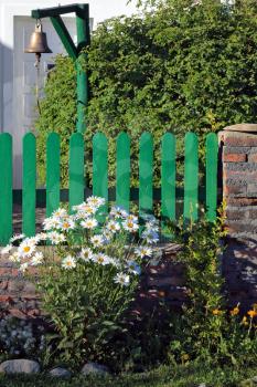 The solitary Estancia in the national park Perito Moreno in Argentina. Bush blooming daisies next to a low fence of green picket fence. Decorative bronze bell