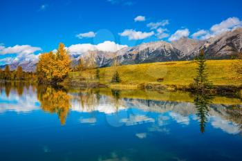 The concept of recreational tourism. Bright shining autumn day in Canmore, near Banff National Park. Scenic cumulus clouds are reflected in the lake