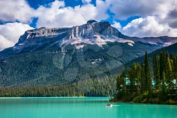 Emerald Lake in the Rocky Mountains of Canada. The green lake surrounded by a coniferous forest. Group of tourists crosses the lake in a rowboat
