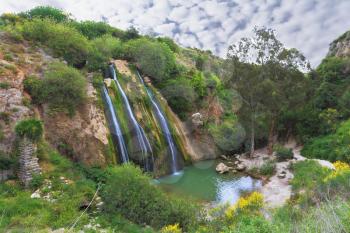 Three parallel streams of water running down the steep slope and fall in oval pool. Unusual three-jet waterfall in northern Israel