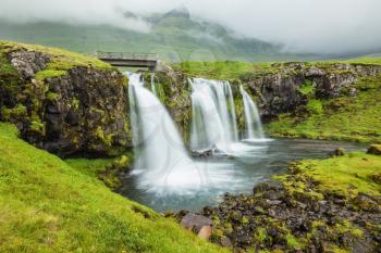 Iceland - country of mountains, rivers and waterfalls. Threaded full-flowing waterfall on the grassy mountains