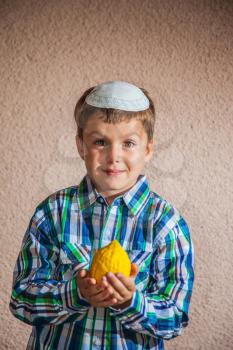 Charming seven year old boy in  white knitted kippah is holding citrus. Citron - ritual fruit for the Jewish holiday of Sukkot