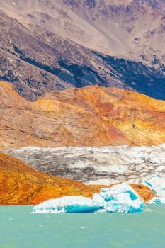 The picturesque multi-colored shore of Lake Viedma. Massive glacier descends into the emerald water. In the water ice-floes, broken away from a glacier