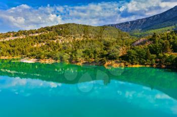 Mountain canyon Verdon in the French Alps. Smooth emerald green water of Lake Sainte-Croix-du-Verdon reflects the sky and wooded shore