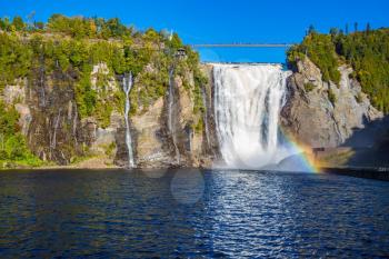 Magnificent rainbow in the waterfall Montmorency in Montmorency Falls Park, in Quebec.  Above the waterfall built bridge for walking. The concept of active and cultural tourism