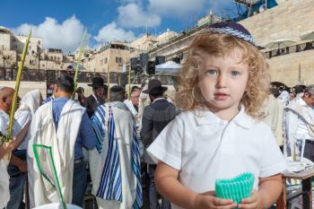 Cute little boy with long blond curls and blue eyes in blue skullcap. He stands at Western Wall of Temple. The Jewish holiday of Sukkot