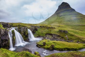 Cascade deep falls on the grassy mountains. Iceland - the country of mountains, the rivers and falls