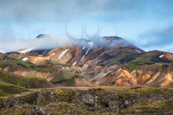  Snow lies in the hollows of multicolored rhyolite mountains. Early summer morning in the National Park Landmannalaugar, Iceland