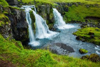 Cascading waterfall Kirkjoufellfoss at the foot of the mountain Kirkjoufell. Summer in Iceland. Concept of exotic and extreme tourism