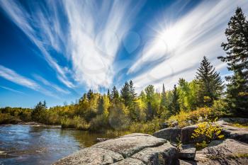 Incredible cirrus clouds  and huge flat stones in Old Pinawa Dam Park. Indian summer in Manitoba, Canada. The concept of ecological and recreational tourism