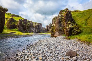 The concept of active northern tourism. Green Tundra in summer. The striking canyon in Iceland. Bizarre shape of cliffs surround the stream with glacial water