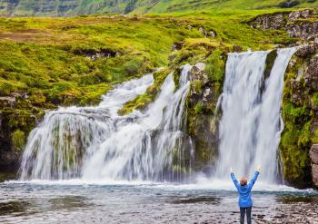 Elderly woman -  traveler enthusiastically raised her hands. Waterfall Kirkjoufellfoss. Summer in Iceland. Concept of exotic and extreme tourism 