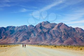  Ecotourism in Africa. Bicycle race in the desert of Namibia. The dirt road in Namib-Naukluft National Park goes to distant mountains