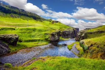 Green Tundra in July. The striking canyon Fyadrarglyufur in Iceland. The concept of active northern tourism. Bizarre shape of cliffs and stream with glacial water