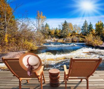 Two deckchairs and hat stand on the shore of the river. Foam water rapids on the smooth stones. Old Pinawa Dam Park, Winnipeg River, Canada. The concept of travel Around the World