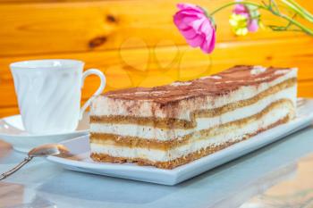 Delicious cake Tiramisu. The background is cup with tea and flowers. Professional bakery