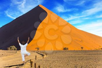 An elderly woman practicing yoga in the desert. Purple and yellow dune of the Namib desert. The concept of extreme and exotic tourism