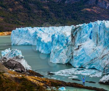 Patagonia. Unique lake and glacier Perito Moreno,  in a mountain valley. Woman -  tourist enthusiastically raised her hands. The concept of  exotic and extreme tourism