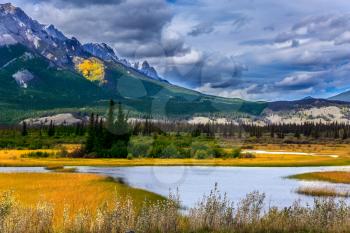 Impressive trip to the Rocky Mountains. Rocks, lakes and yellow grass under flying clouds. Concept of active automobile and ecological tourism