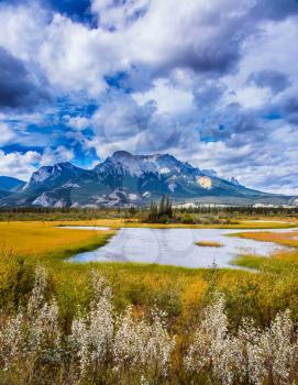 Impressive trip to the Rockies of Canada. Rocks, lakes and yellow grass under flying clouds. Concept of active automobile and ecological tourism
