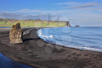 Cape Dirholaey in southern Iceland. On the beach with black volcanic sand is a huge rock in the shape of palms