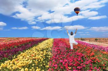 Buttercups blooming garden. An elderly woman dressed in white doing yoga pose Tree. Balloon flies over a field