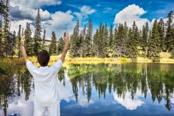 Jasper National Park in the Rocky Mountains of Canada. Patricia Lake. Middle-aged woman, dressed for yoga, Sun Salutation on the shore of small lake