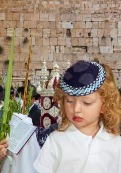Handsome little boy with blond side curls and blue eyes, in skullcap. Western Wall of the Temple. The Jews brought the Torah Scroll for prayer. Autumn Jewish holiday Sukkot