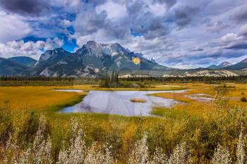  Cloudy Indian summer in the Rockies of Canada. Rocks, lakes and yellow grass under flying clouds. Concept of active automobile and ecological tourism