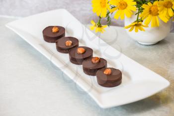 Gonfectionery desserts. Portion small chocolate cakes are decorated with nuts. Background -  white vase with field chamomiles. Professional bakery
