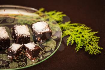 Professional baking. Portioned chocolate desserts sprinkled with coconut shavings. Beautiful translucent plate with patterns. Background brown