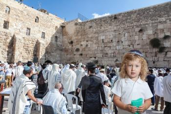 The Jewish holiday of Sukkot. Cute little boy with long blond curls and blue eyes in blue skullcap. He stands at Western Wall of Temple