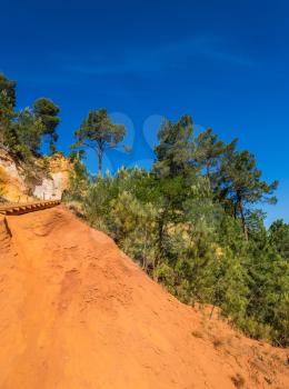 Unique red and orange hills in the province of Roussillon, France. Coniferous forests create a beautiful contrast with the color of ocher