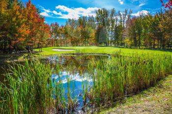 Concept of recreational tourism. Shining day in French Canada.  Autumn foliage reflected in clear water of the pond. Charming pond in the picturesque park