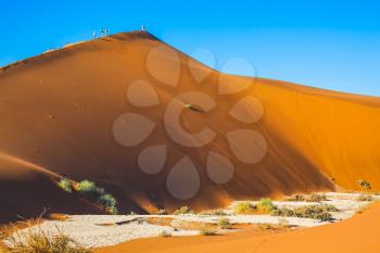 Travel to Namibia. Namib-Naukluft National Park. Tourists and photographers climb the sharp ridge of high dunes