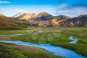 Snow lies in the hollows of colorful rhyolite mountains. Green Valley is flooded with melt water.  Early summer morning in the National Park Landmannalaugar, Iceland