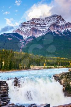 Canada, Jasper National Park. Powerful picturesque waterfall Athabasca. Gorgeous pyramidal mountain covered with the first snow