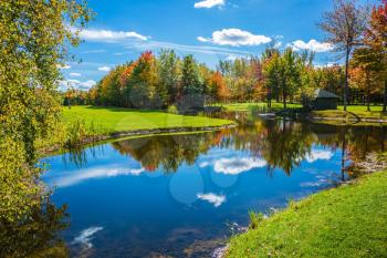  Concept of recreational tourism. The shining sunny day in the French Canada. Park of fantastic beauty. Red, orange and yellow autumn foliage is reflected to clear water of the lake