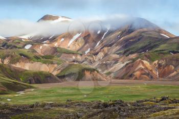  Snow lies in the hollows of multicolored rhyolite mountains. Early summer morning in the National Park Landmannalaugar, Iceland