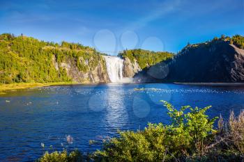 Sunny autumn day. The vast blue lake and powerful waterfall Montmorency in Montmorency Falls Park, in vicinities Quebec. The concept of active and cultural tourism
