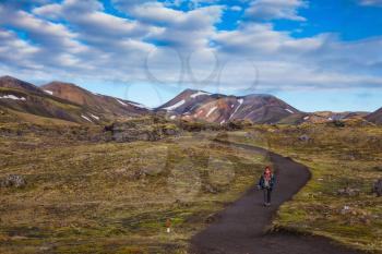 The woman - tourist goes on a footpath. Summer trip to Iceland. Valleys and Mountains National Park Lanmannalaugar