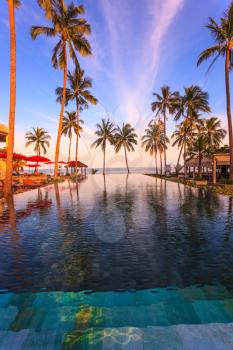  Pool surrounded by palm trees on the sea beach. On the edge of the pool red sun canopy. Rest of the Andaman Sea. Popular resort on Koh Samui