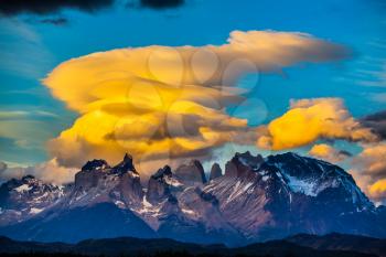  The black-and-steel color of the cliffs of Los Cuernos. Magnificent orange clouds in the rays of the sunset. The concept of extreme and active tourism. Torres del Paine National Park