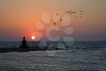 Silhouette of woman practising yoga and meditating on sunrise