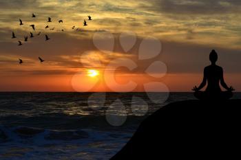 Woman silhouette meditating in a yoga pose on the beach at sunrise