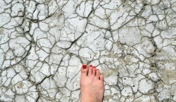 Top view of woman leg with red nail polish on drought land, climate change