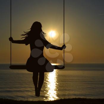 A young woman silhouette who is swinging at the sea shore whaching sunrise