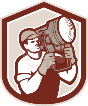 Illustration of a electrical lighting technician crew carry fresnel spotlight on shoulder looking to side set inside shield crest shape on isolated background done in retro style.