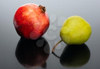 Royalty Free Photo of a Pomegranate and a Pear Reflected on Black